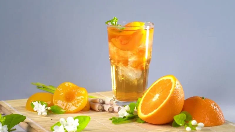 Top 5 quán cafe phường Minh Phụng đáng ghé Ly trà đào cam sả đựng đá viên và đào miếng mọng nước, đặt trên mẹt tre nhỏ cùng nửa quả cam, vài nhánh sả và hoa nhài trắng trang trí