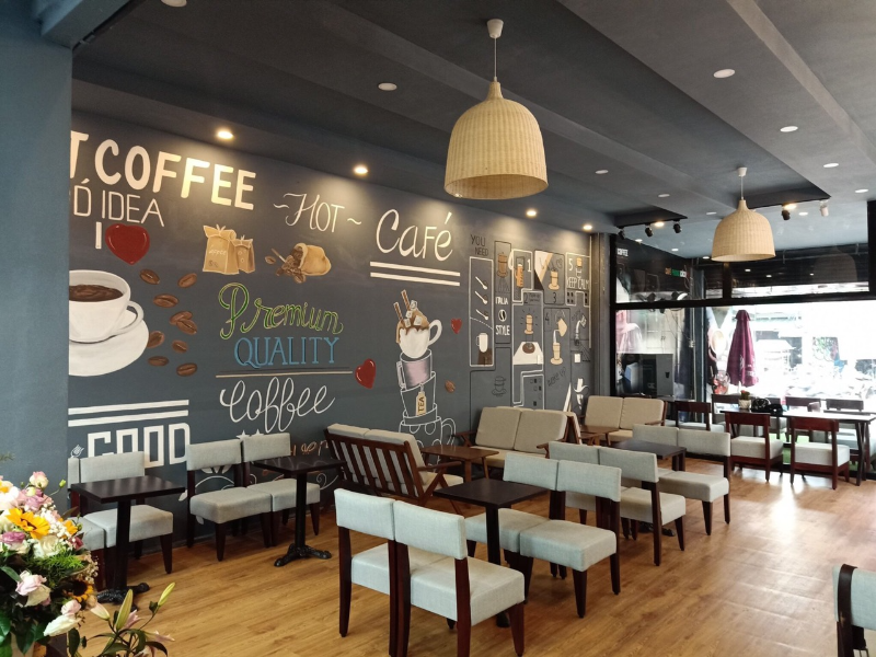 Không gian quán cà phê hiện đại với tường vẽ nghệ thuật chủ đề cà phê và bàn ghế sofa xám
