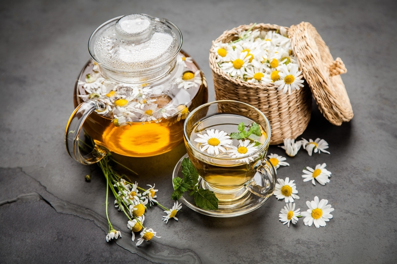 Set trà hoa cúc nóng thanh tao gồm ấm trà và tách trà thủy tinh bày trí cạnh giỏ mây cúc khô