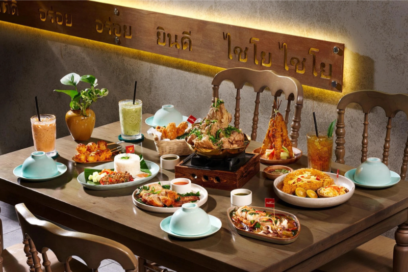 Bàn tiệc ẩm thực Thái Lan đa dạng với xôi cháy gà quay, thịt xiên nướng, gỏi và nước trà sữa Thái trên bàn gỗ