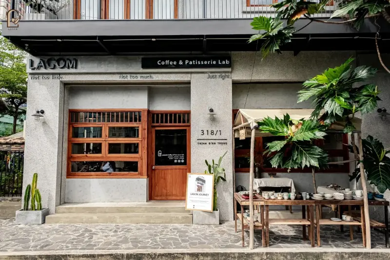 Phong cách tối giản của quán Lagom Coffee và Patisserie Lab tại số 318/1 Trịnh Đình Trọng với cửa gỗ, tường xám và quầy bày bán đồ gốm ngoài trời. Gợi ý lý tưởng khi bạn băn khoăn chơi gì ở phường Tân Phú.