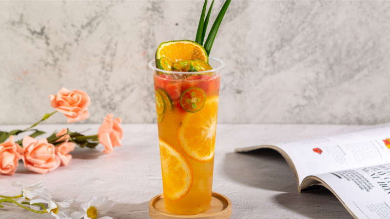 Ly nhựa chứa trà trái cây nhiệt đới với các lát cam dâu tây và tắc tươi trang trí lá dứa - thức uống giải khát