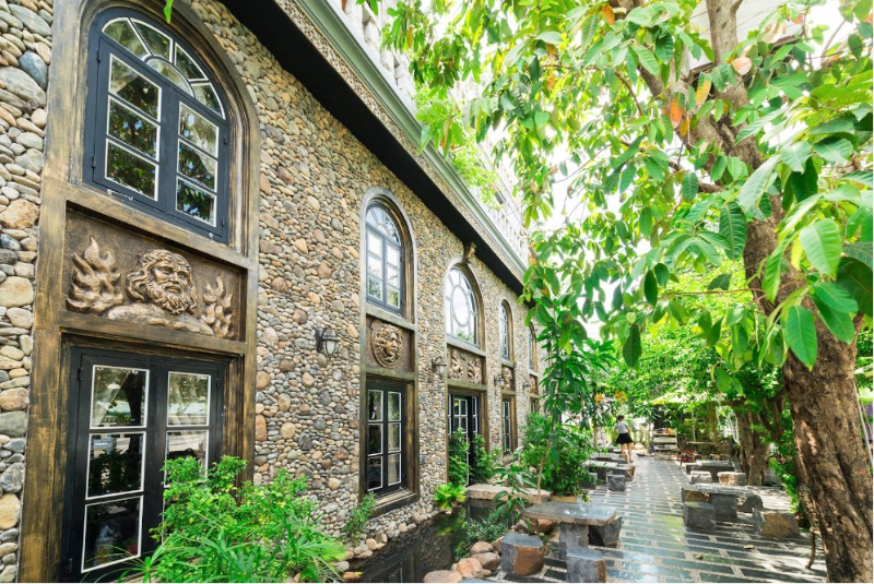 Không gian sân vườn quán cà phê tường ốp đá cuội kiểu La Mã với cửa vòm và cây xanh