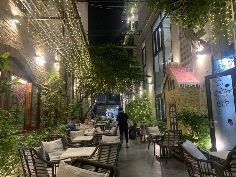 Top 15 quán cafe phường Tân Sơn Nhì có không gian đẹp Không gian sân vườn quán cà phê lung linh ban đêm với dải đèn dây treo ấm áp và ghế mây