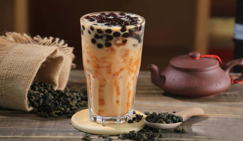 Ly trà sữa trân trùng đường đen hấp dẫn đặt cạnh ấm trà sứ và hạt trà khô