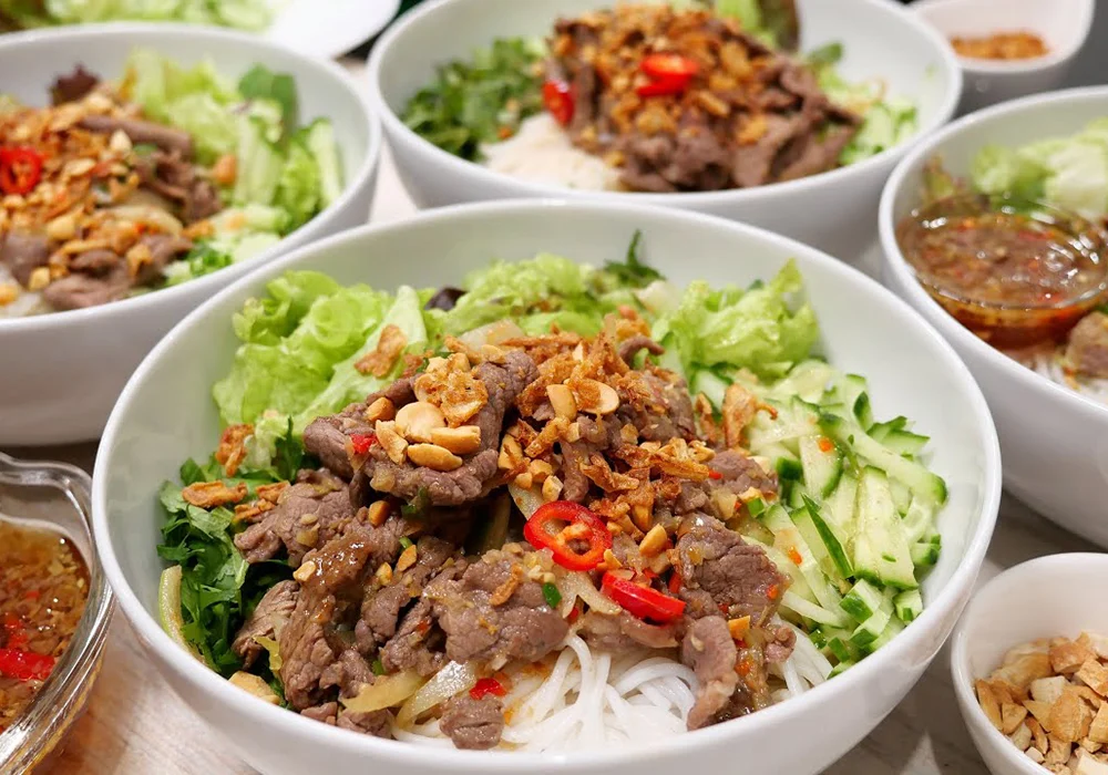 Top 15 quán ăn ngon phường Đông Hưng Thuận đáng ghé thử Các bát bún trộn thịt bò nam bộ tại quán ăn ngon phường Đông Hưng Thuận, với thịt bò xào thơm, bún tươi, rau sống, dưa chuột thái sợi, lạc rang và nước chấm chua ngọt được múc ra bát nhỏ bên cạnh