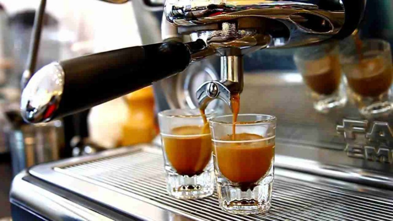 Máy pha cà phê chuyên nghiệp đang chiết xuất dòng espresso có lớp crema vàng đậm đà, chảy đều vào hai ly thủy tinh nhỏ đặt phía dưới