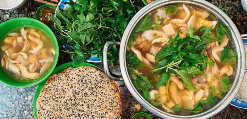 Nồi lẩu gà lá é sôi sùng sục ăn kèm rau thơm và bánh tráng mè đen
