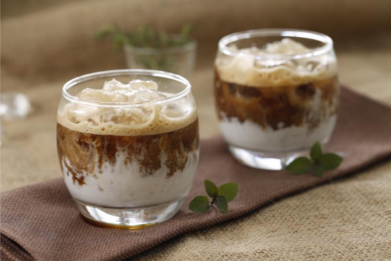Hai ly cà phê đen đá và bạc xỉu nhiều sữa sủi bọt vàng óng trên khay gỗ tại quán cafe
