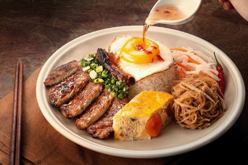 Đĩa cơm tấm sườn nướng, chả trứng và trứng ốp la đang rưới nước mắm