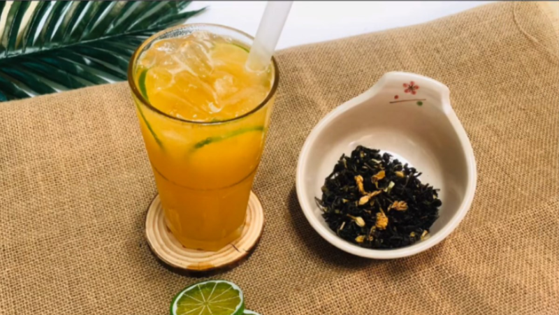 Ly trà trái cây nhiệt đới màu vàng cam rực rỡ bên cạnh chén trà khô thơm ngát