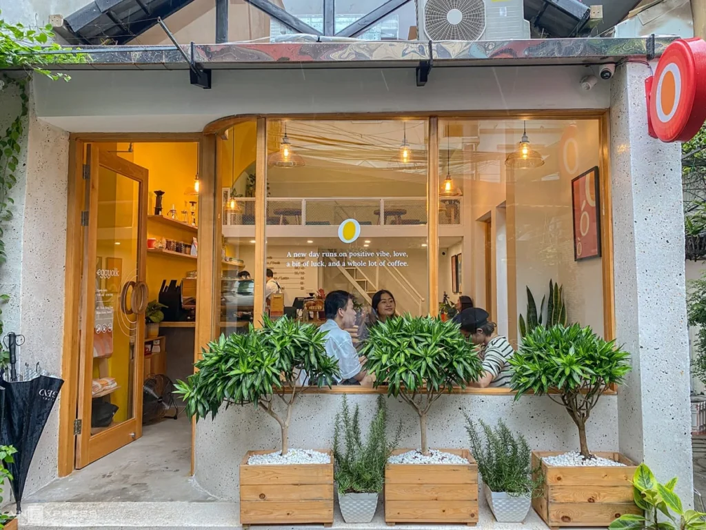 Top 15 quán cafe phường Tây Thạnh không gian đẹp không thể bỏ lỡ Cửa hàng cà phê Eggyolk mặt tiền mộc mạc với cửa kính lớn và cây xanh trang trí trước hiên