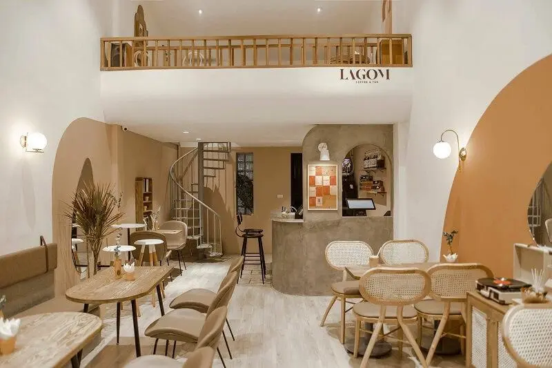 Chơi gì ở phường Tân Phú sau sáp nhập để có trải nghiệm vui? Quán cà phê Lagom Coffee & Tea, một không gian ấm cúng với tông màu nâu và be chủ đạo. Có một gác lửng với lan can gỗ nhìn xuống tầng trệt. Cầu thang xoắn ốc bằng sắt dẫn lên gác lửng. Nhiều bàn ghế gỗ và ghế mây được sắp xếp gọn gàng.