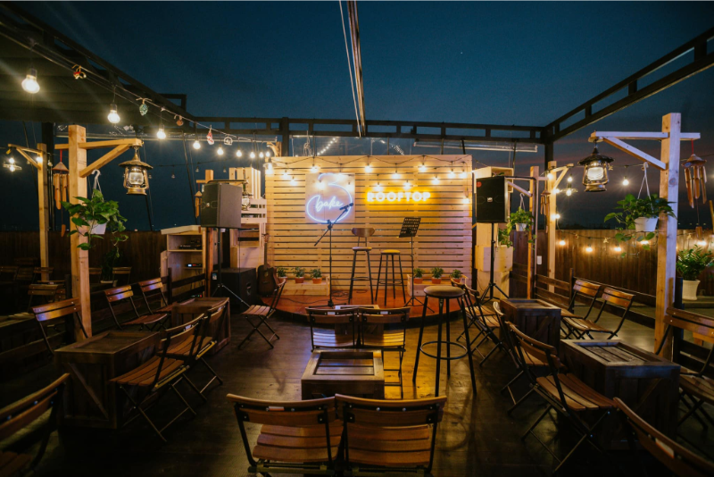 Không gian quán Bake rooftop sân thượng ban đêm lung linh ánh đèn với sân khấu nhạc acoustic.