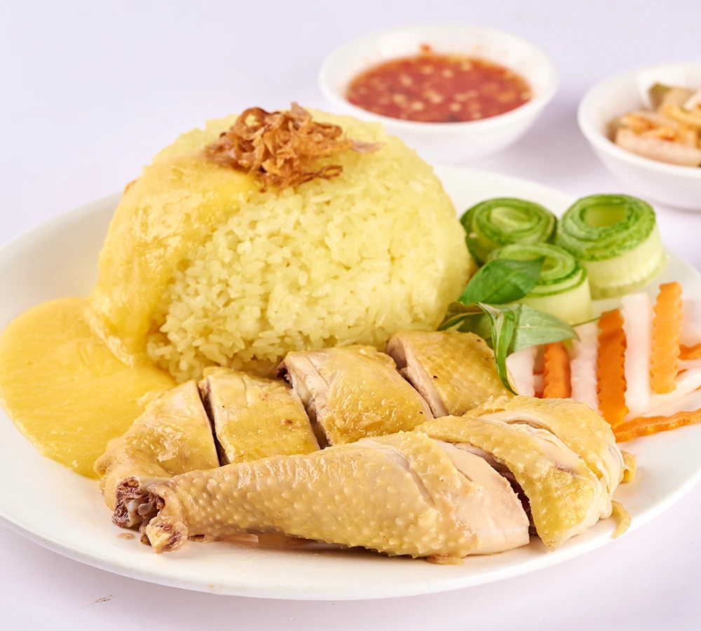 Đĩa cơm gà luộc vàng ươm ăn kèm salad rau củ, bát nước dùng và chén nước chấm