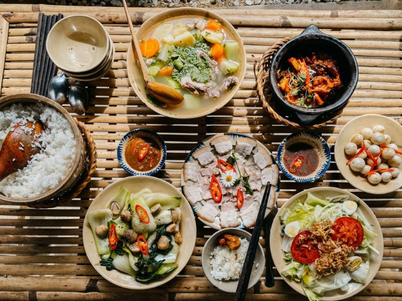 Mâm cơm gia đình truyền thống bày trên bàn tre gồm thịt luộc, canh sườn hầm củ quả và cá kho tộ